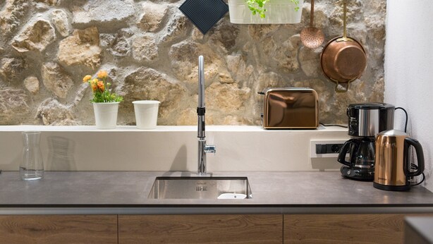 A kitchen with a stone wall, a sink, hanging pots, a coffee maker, and a plant. - BASTINICA KRK Studio Ap 1, OldTown, CityCenter (Krk)