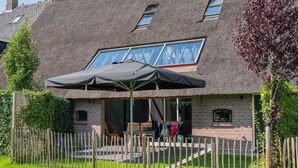 Een gebouw met rieten dak, een overdekt terras, een houten omheining en een gazon.