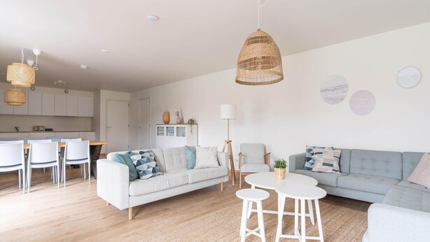 A modern living room with a sofa, two white tables, and a dining area with chairs.