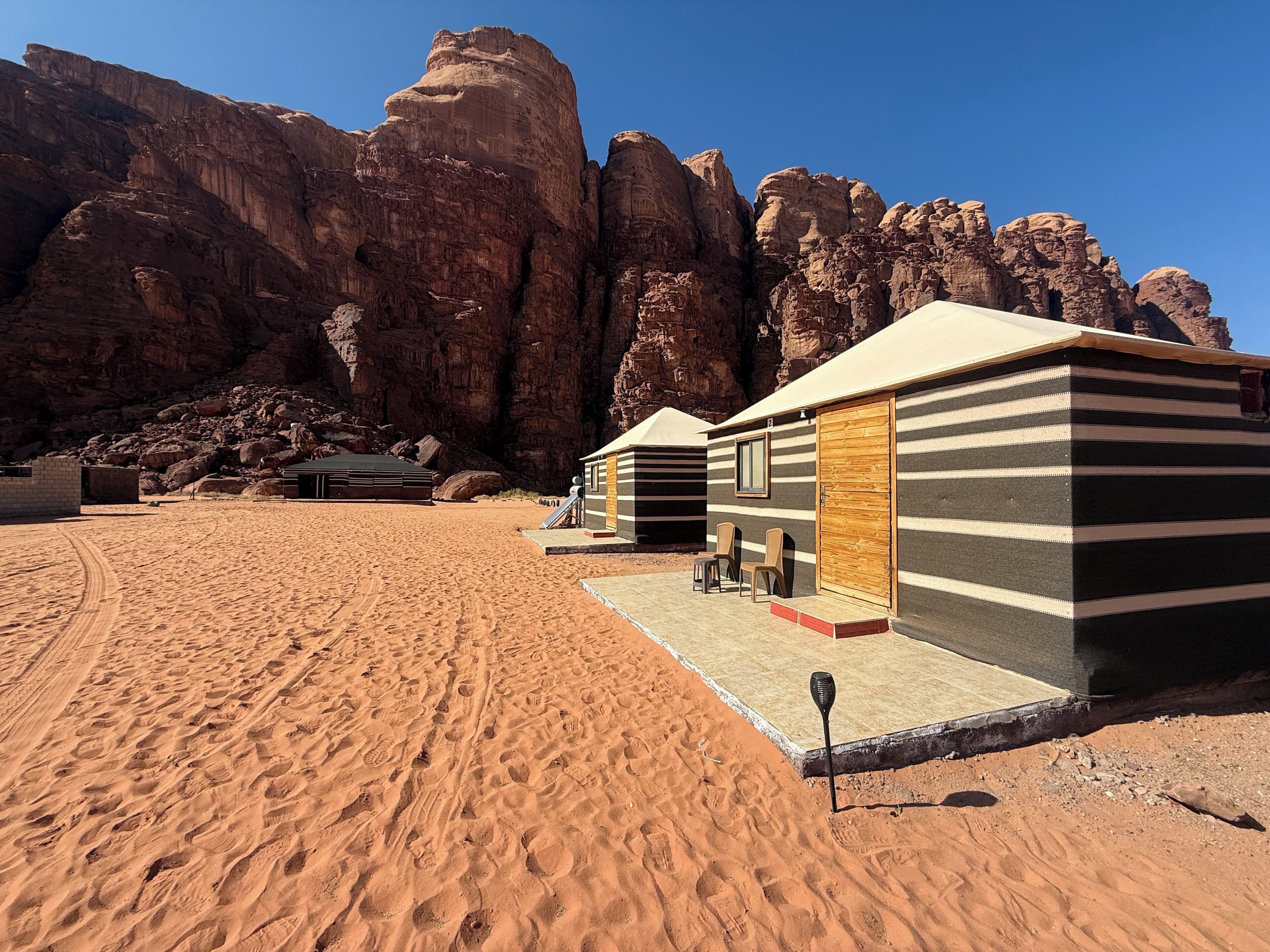 A desert landscape with a small building featuring a striped exterior and a wooden door.