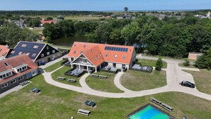 An aerial view of a residential area with a large house featuring a red-tiled roof, a swimming pool, and a tennis court.