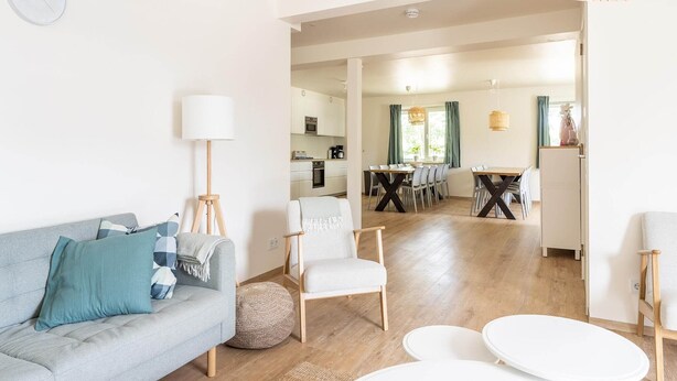 A modern living room with a sofa, armchair, and round tables. A kitchen and dining area are visible in the background.