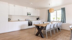A modern kitchen with white cabinets, a wooden dining table, and a large window with curtains.
