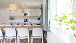 A modern kitchen with white cabinets, a wooden dining table, and two hanging wicker chandeliers.