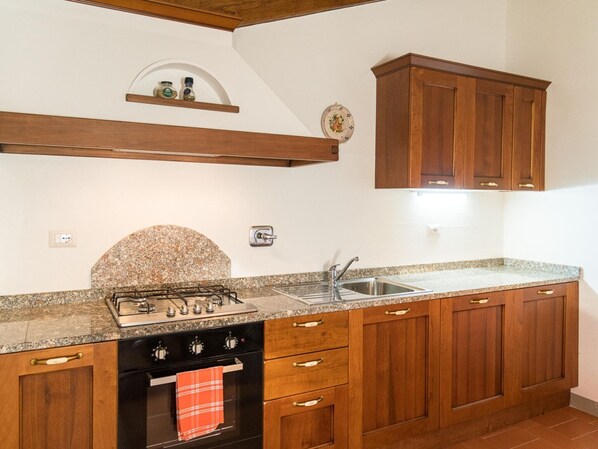 Una cocina con encimeras de granito, armarios de madera, horno empotrado y pileta de acero inoxidable.