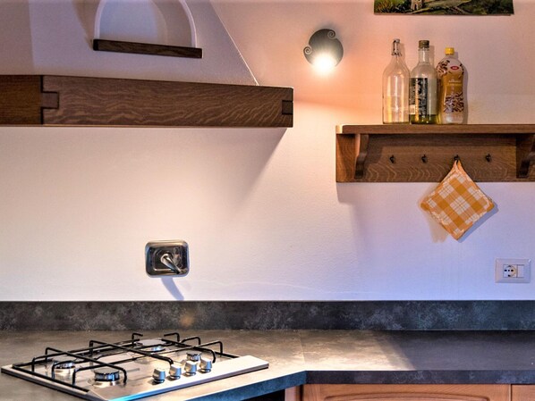 Una cocina moderna con estufa a gas, estantes de madera y una lámpara fijada a la pared.