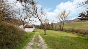 A rural path leading to a white building with a red-tiled roof, surrounded by trees and open fields. - Belvilla by OYO Casa Ca Rio (Marche)