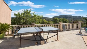 Ein Tischtennis-Tisch steht auf einer Terrasse mit Blick auf einen Berg und Bäume.