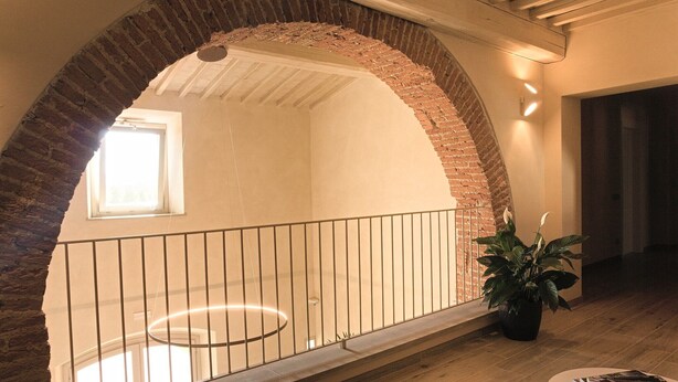 Una habitación amplia con techo alto, un arco de ladrillo, un balcón con barandilla y una planta en maceta.