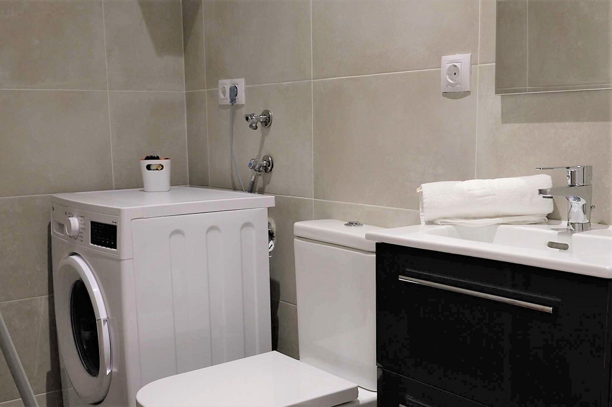 Une petite salle de bain équipée d’un lave-linge, de toilettes et d’un lavabo.