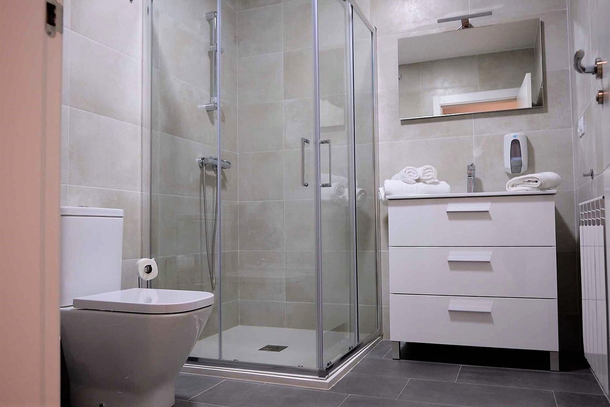 Un baño moderno con ducha de vidrio, inodoro y tocador con espejo y perchero.