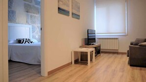 Una habitación moderna con una cama, televisión, una mesita y un sofá.