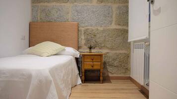 A small, neatly arranged bedroom with a bed, a nightstand, and a stone wall.