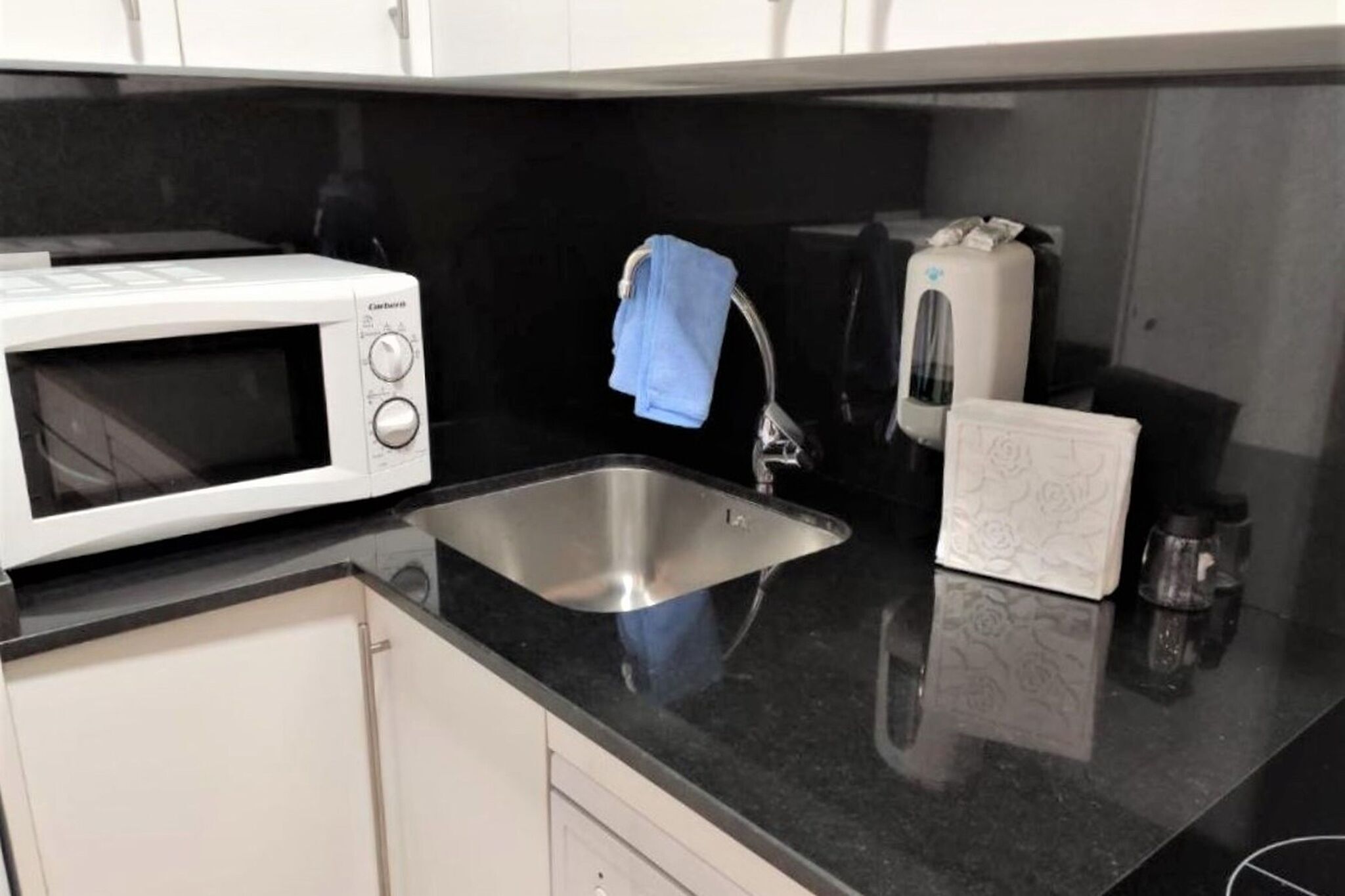 Une cuisine équipée d’un four à micro-ondes, d’un évier, d’une serviette accrochée au robinet, d’un grille-pain et d’une boîte de mouchoirs.