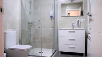 Un baño moderno con ducha de vidrio, inodoro blanco y tocador con espejo.