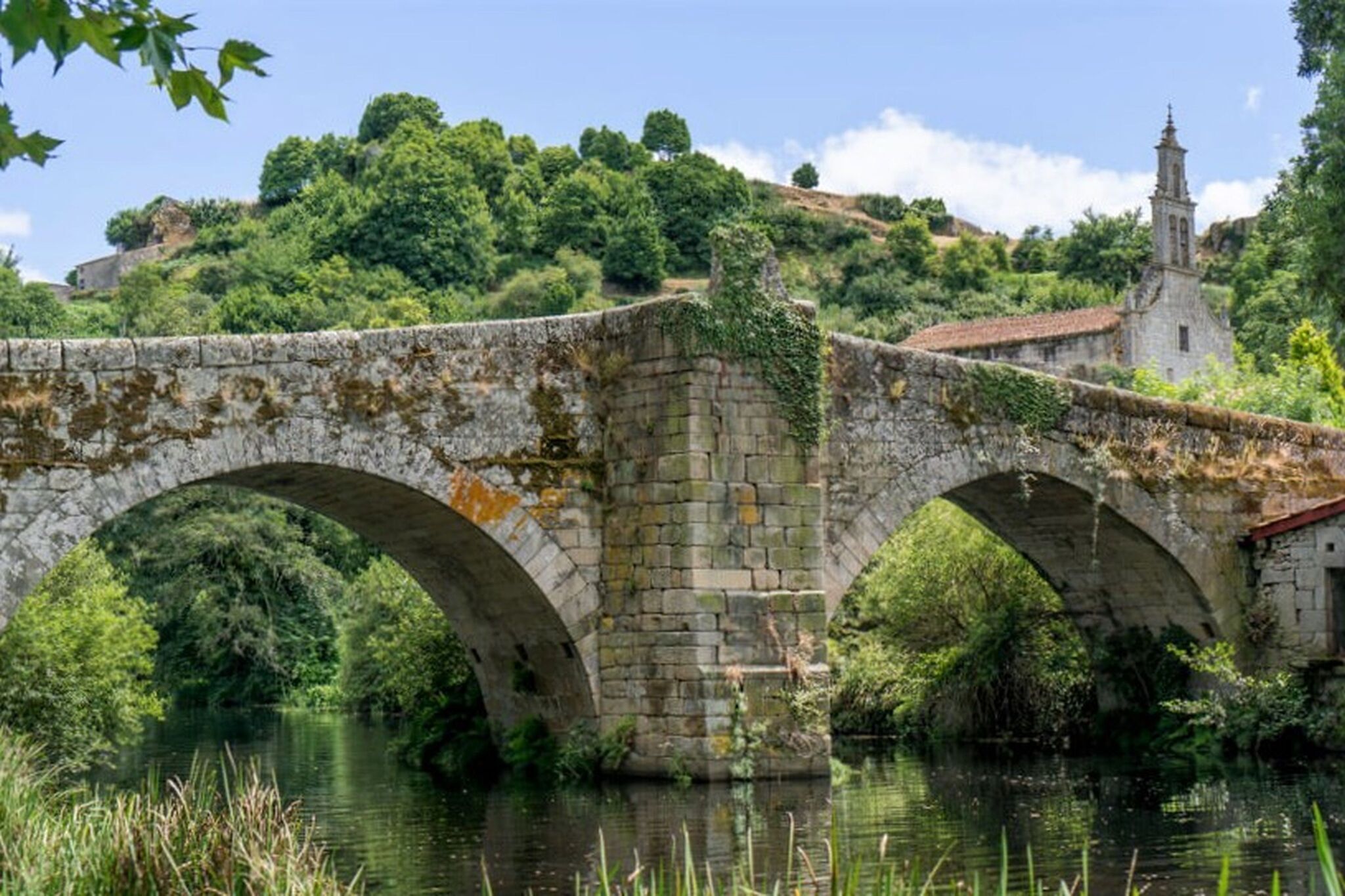 Un puente de piedra sobre un río, con una iglesia al fondo.