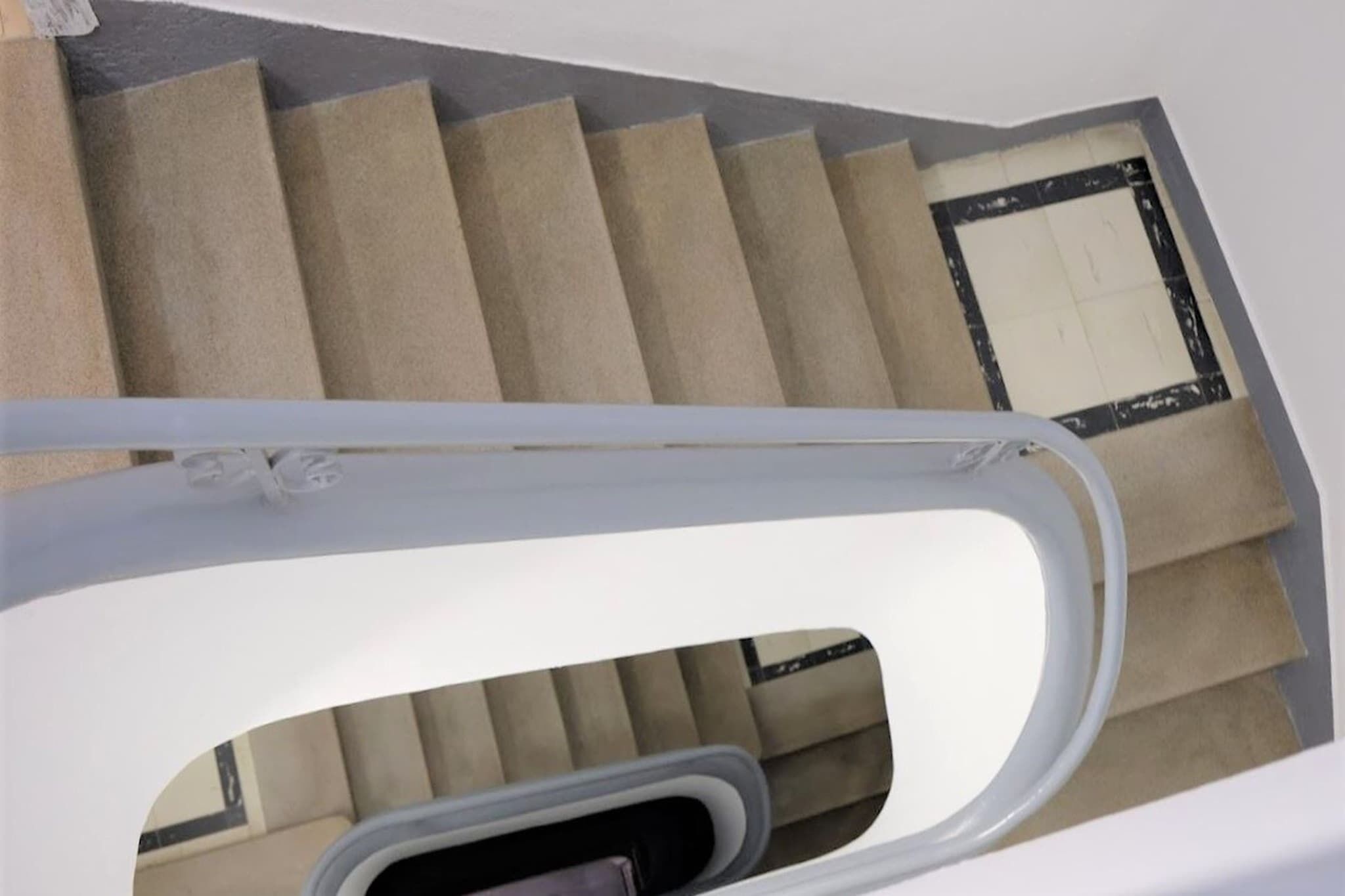 A staircase with beige carpeted steps and a white handrail.