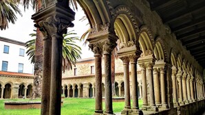 Un patio con una serie de columnas y arcos, un edificio al fondo y una palmera.