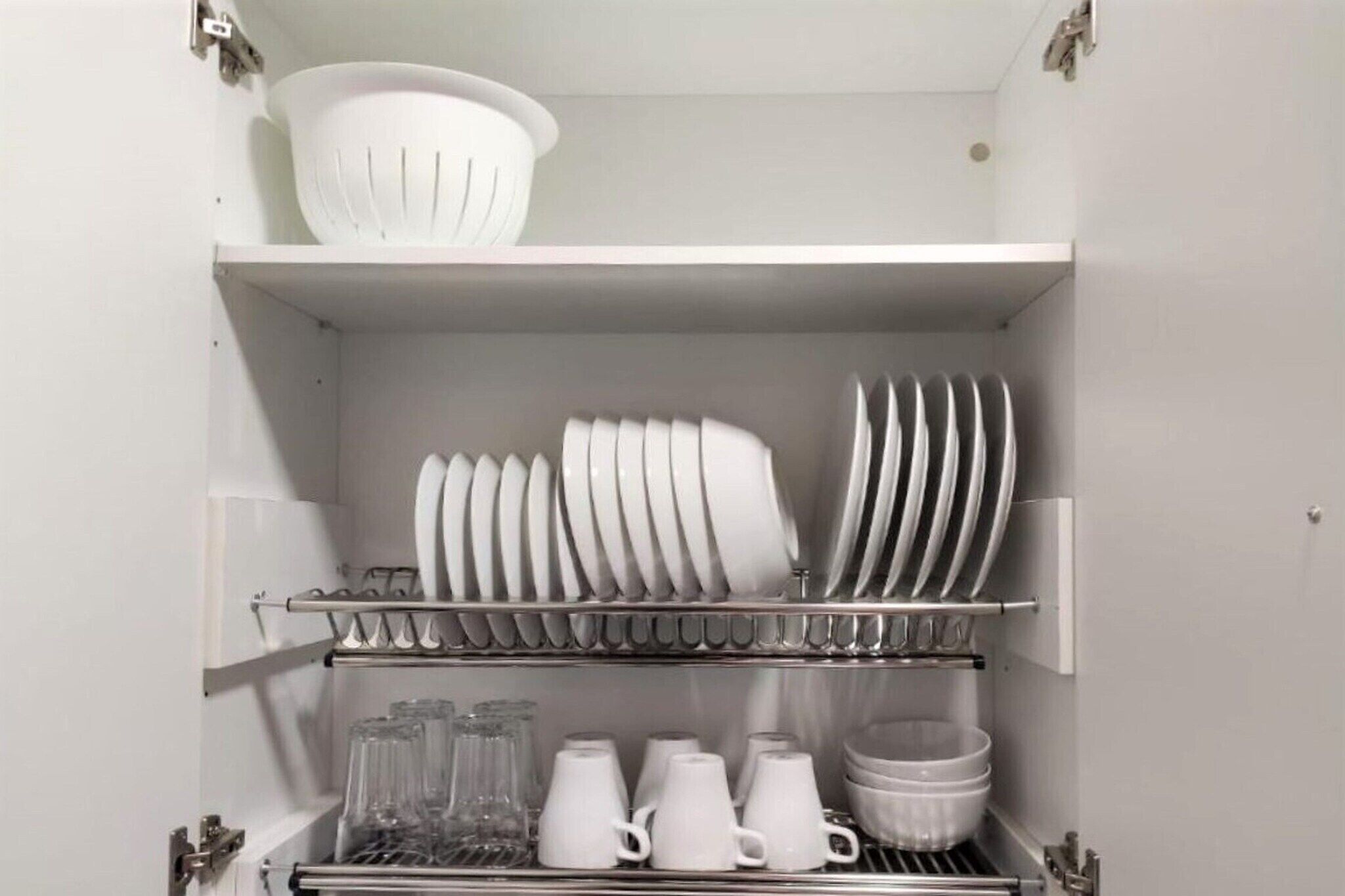 Una cocina con estantes que contienen platos blancos, vasos y un colador.