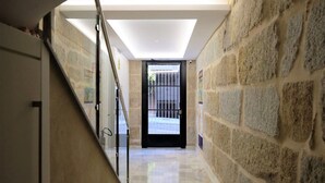 Un pasillo con paredes de piedra, baranda de cristal y puerta que da al exterior.