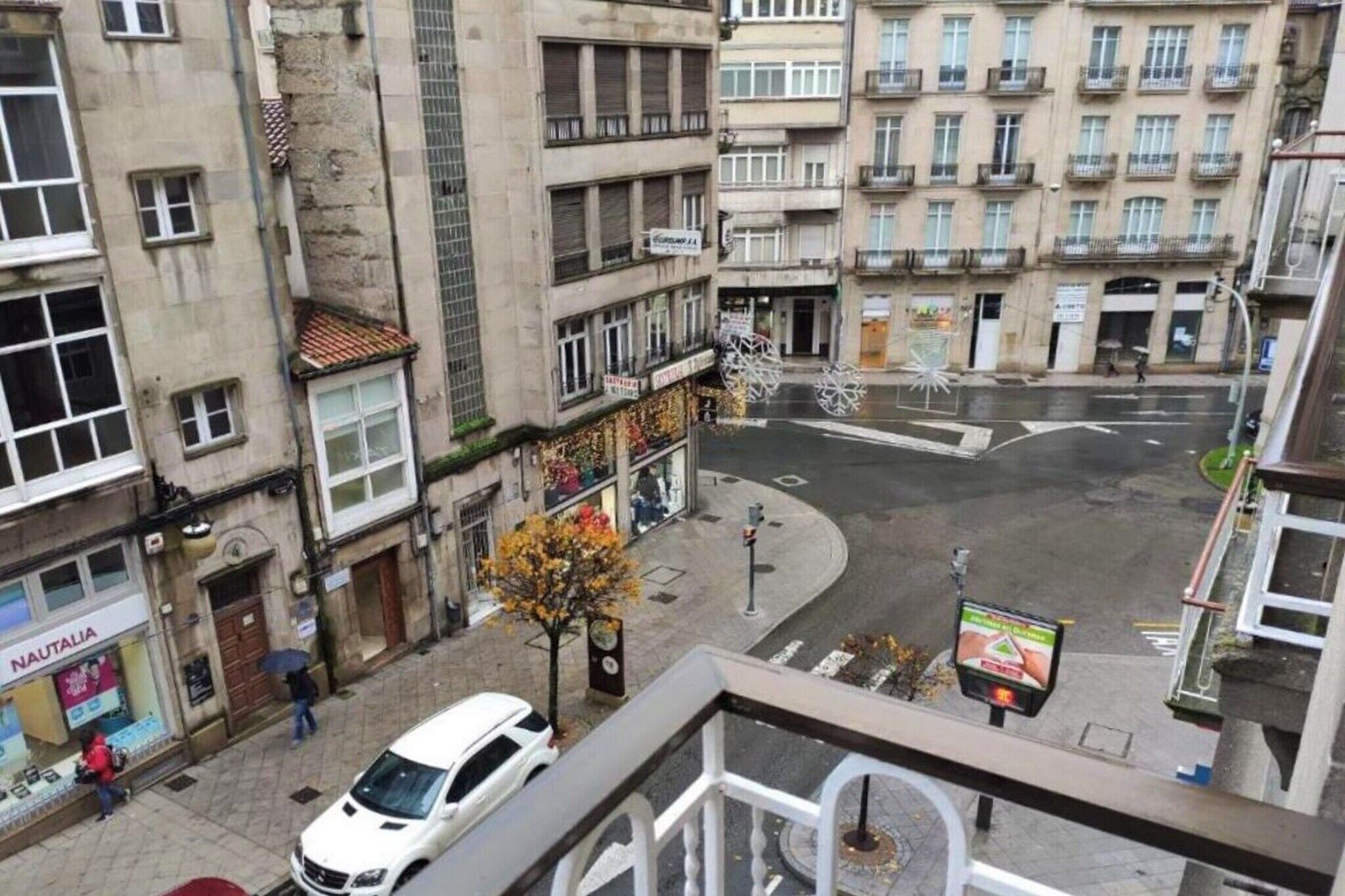 A street view with a white car parked on the side, buildings with balconies, and a pedestrian crossing.