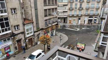 A street view with a white car parked on the side, buildings with balconies, and a pedestrian crossing.