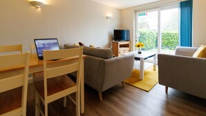 A modern living room with a sofa, a dining table with chairs, a TV on a stand, and a large window with curtains. - Lolite Apartment in Cambridge (Cambridge)