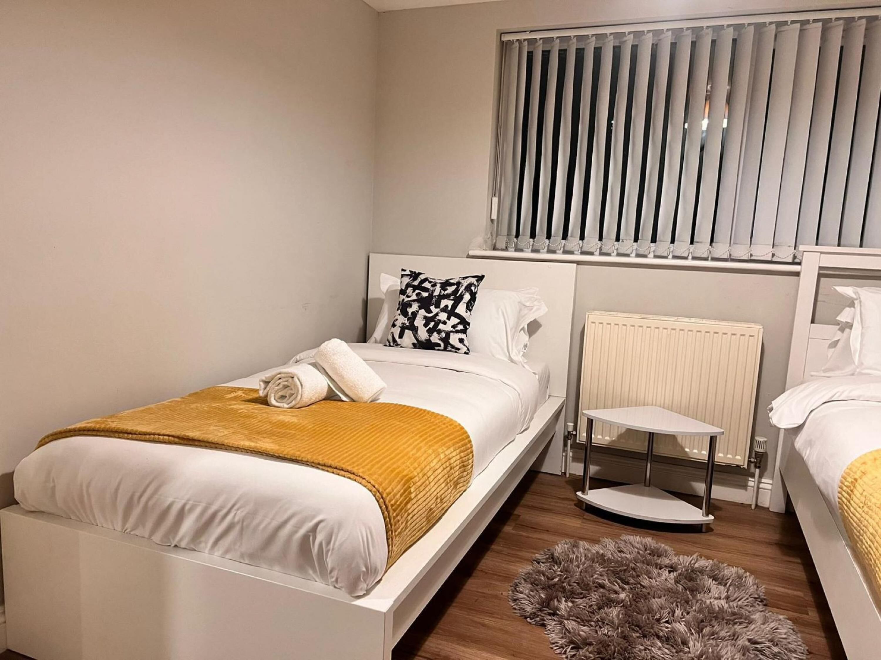 Une chambre avec un lit simple, une table de chevet, un radiateur et une fenêtre avec des stores.