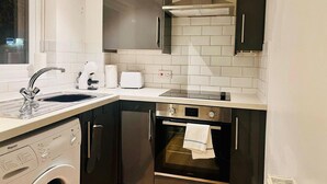 A compact kitchen with a washing machine, a built-in oven, and a stainless steel range hood. - Lolite Apartment in Cambridge (Cambridge)