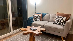 A living room with a grey sofa, two patterned cushions, a wooden coffee table, and a large window with a curtain. - Lolite Apartment in Cambridge (Cambridge)