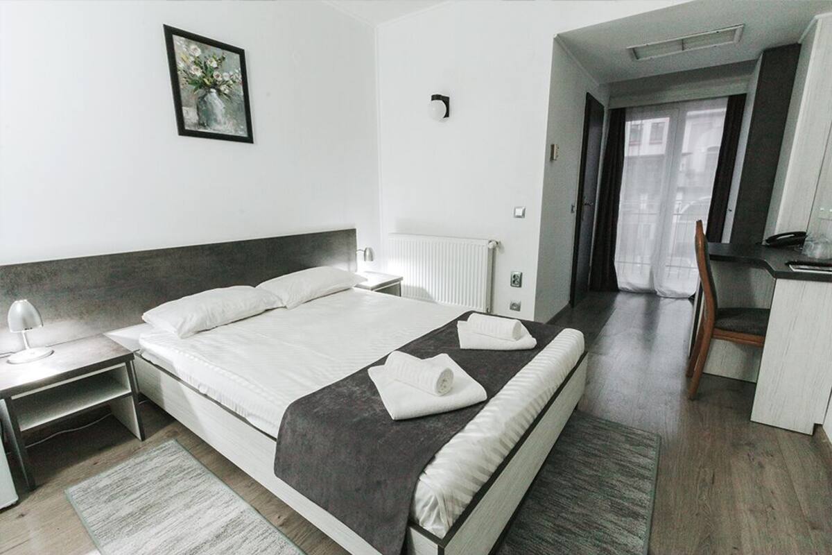 Ett modernt hotellrum med en stor säng, ett sängbord, en stol och utsikt över staden genom fönstret.