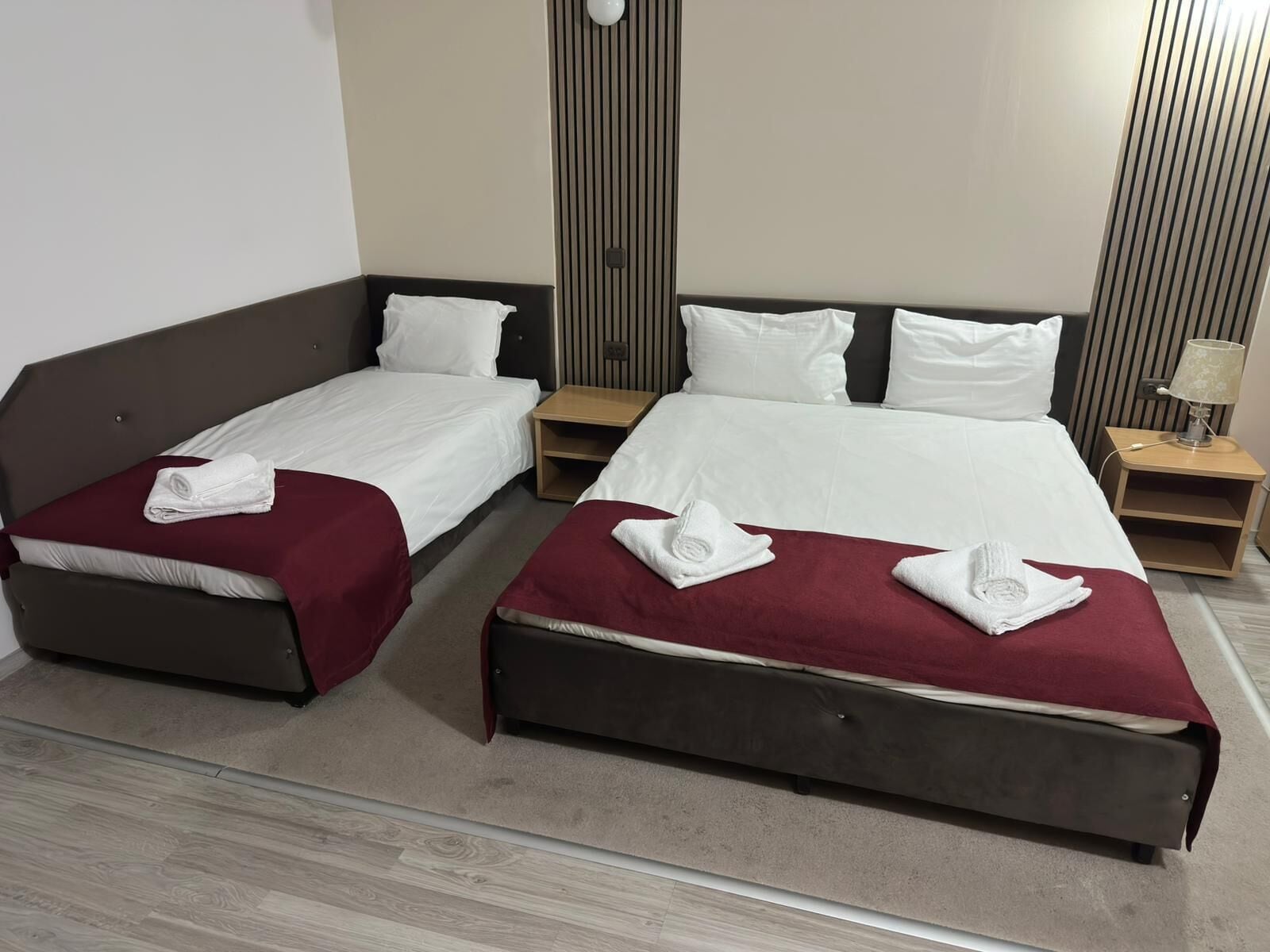 A hotel room with two beds, each with a red bedspread and white pillows. There are wooden nightstands with lamps, and the walls have vertical paneling.