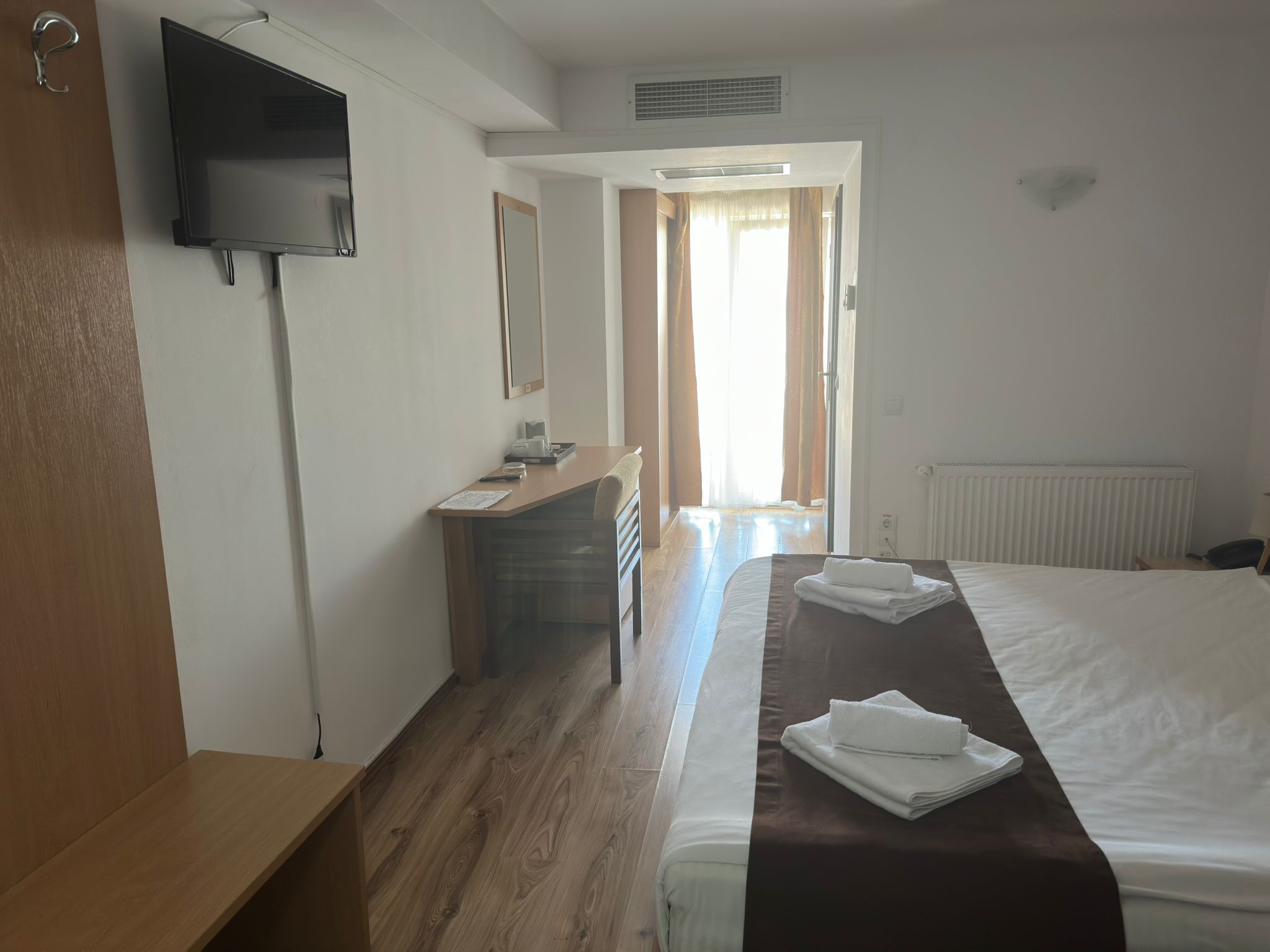 A hotel room with a bed, a desk, a chair, a television, and a window with curtains.