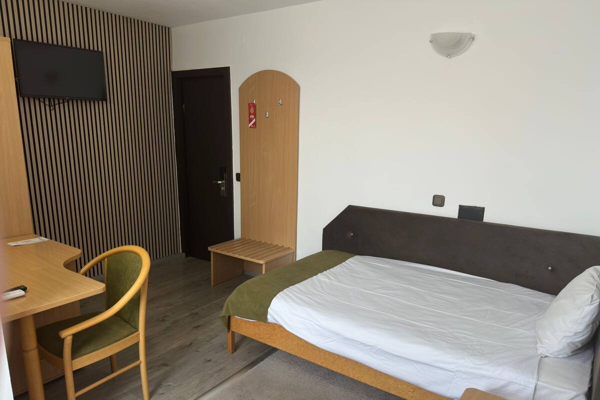 Ett hotellrum med en säng, ett skrivbord, en stol, en tv och en garderob.