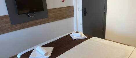 A hotel room with a bed, a TV mounted on the wall, a wooden panel, and a door.