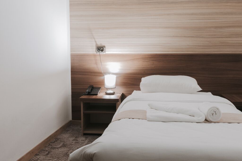 Une chambre d’hôtel avec une tête de lit en bois, une table de chevet avec une lampe, un téléphone et des serviettes soigneusement pliées.