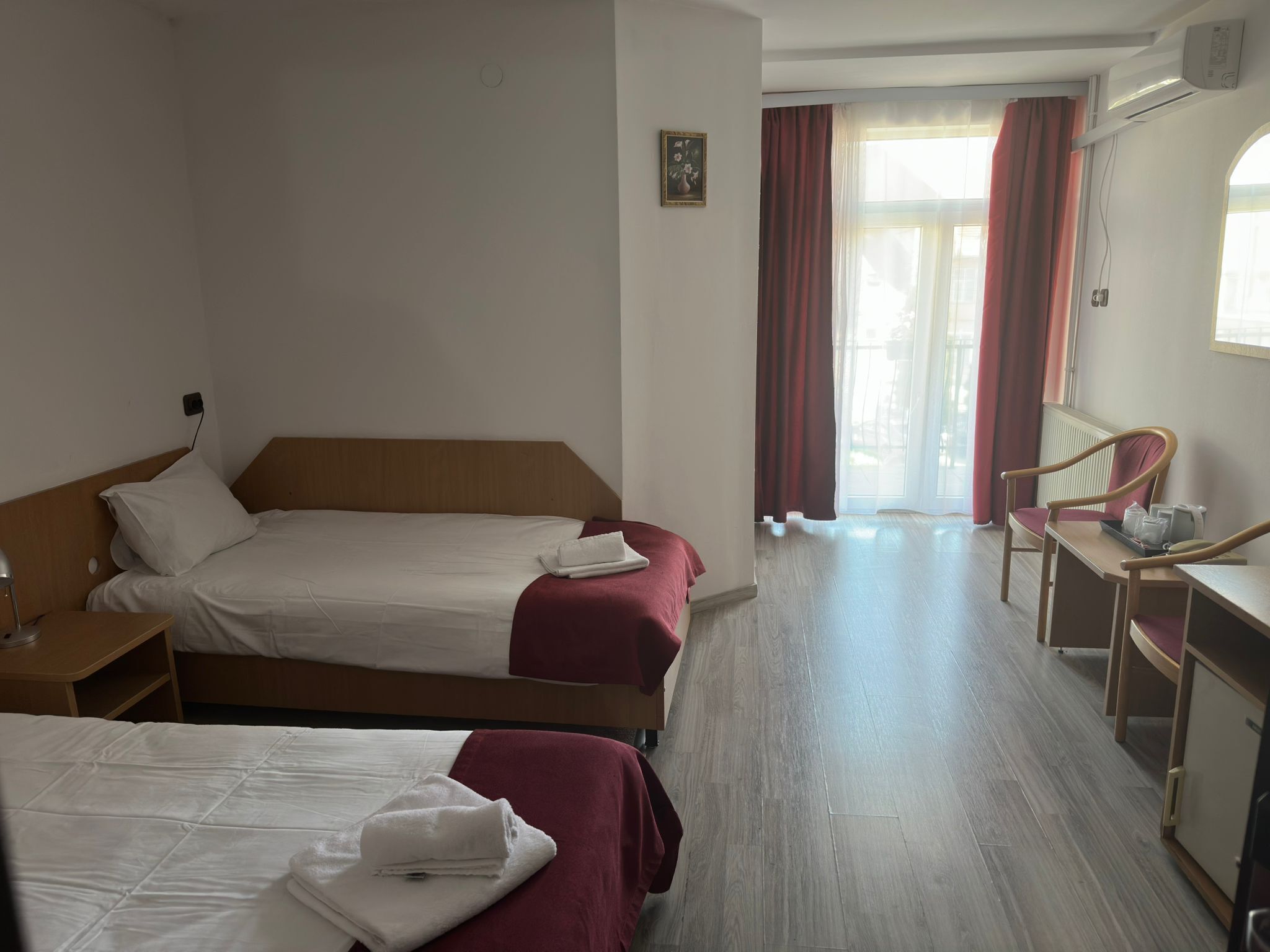 A hotel room with two beds, a desk, a chair, and a window with curtains.