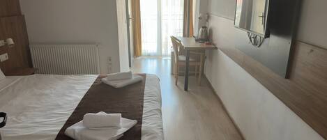Habitación de hotel con cama, escritorio, silla, televisión y ventana con cortinas.