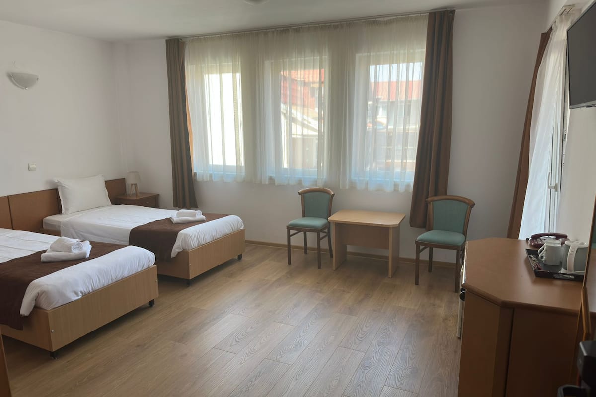 Ett hotellrum med två separata sängar, ett litet bord, två stolar och ett skrivbord med en telefon och en kaffebryggare.