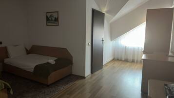 A hotel room with a bed, a desk, a chair, a door, and a window with curtains.
