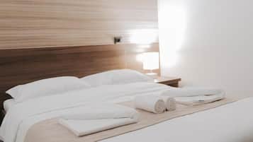 A neatly made bed with white linens and rolled towels, a wooden headboard, and a bedside table with a lamp.