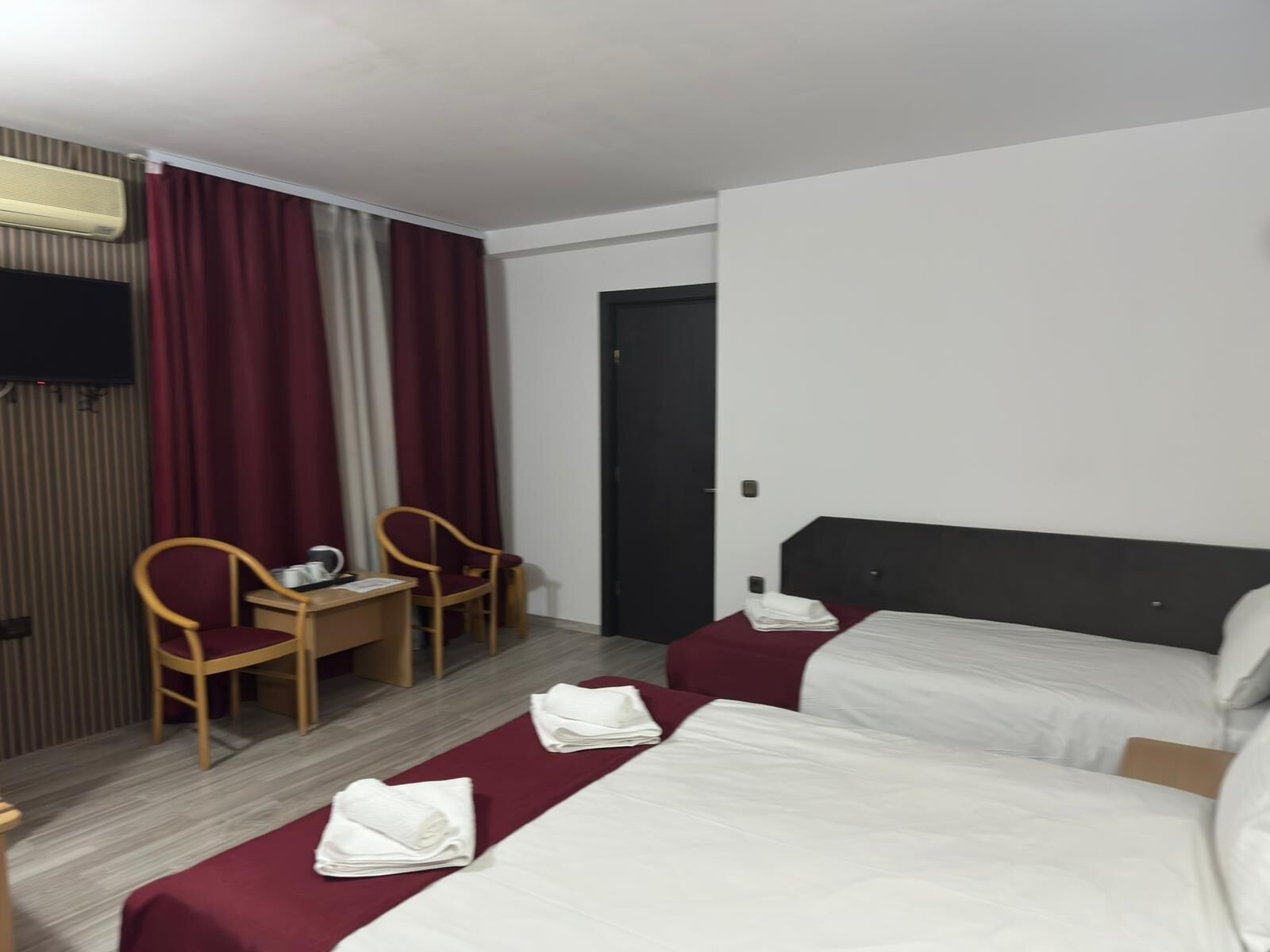 Ein Hotelzimmer mit zwei Betten, einem Schreibtisch, zwei Stühlen, einem Fernseher und einer Tür.