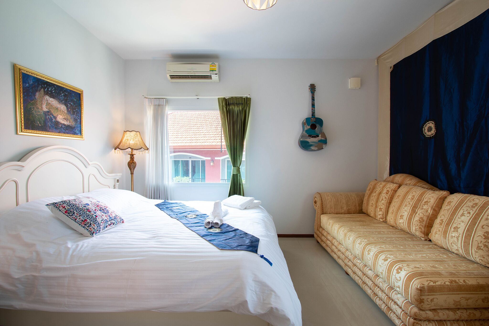 Een hotelkamer met een bed, een slaapbank, een gitaar en een schilderij aan de muur.