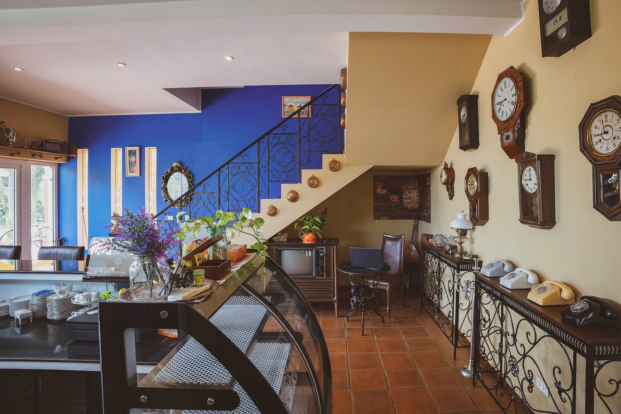 A dining area with a staircase, a TV, and a collection of clocks on the wall.