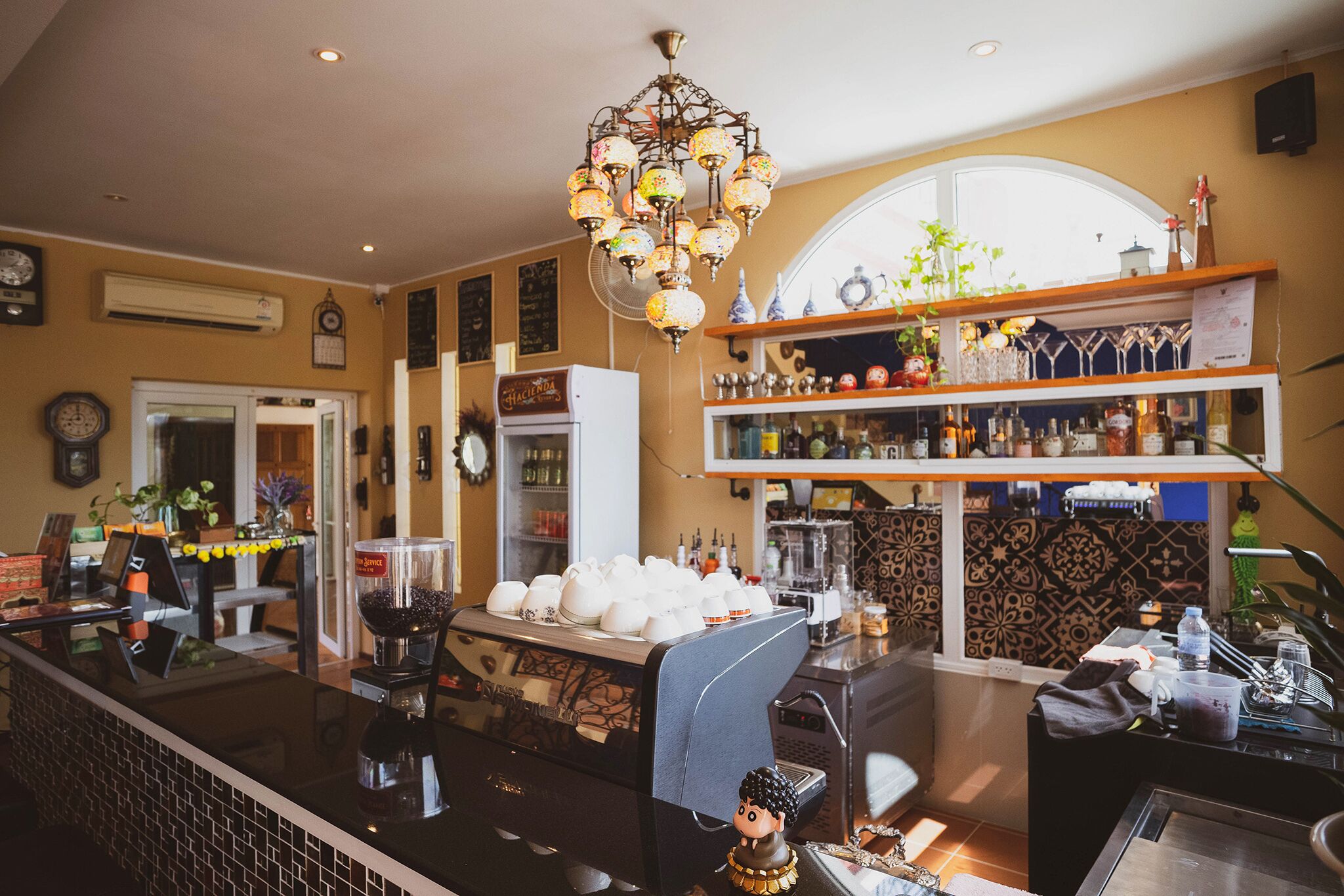 Uma área de bar com máquina de café, prateleiras com garrafas e um lustre decorativo.