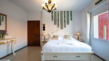 A neatly arranged bedroom with a large bed, bedside lamps, a chandelier, and a view of the outdoors.