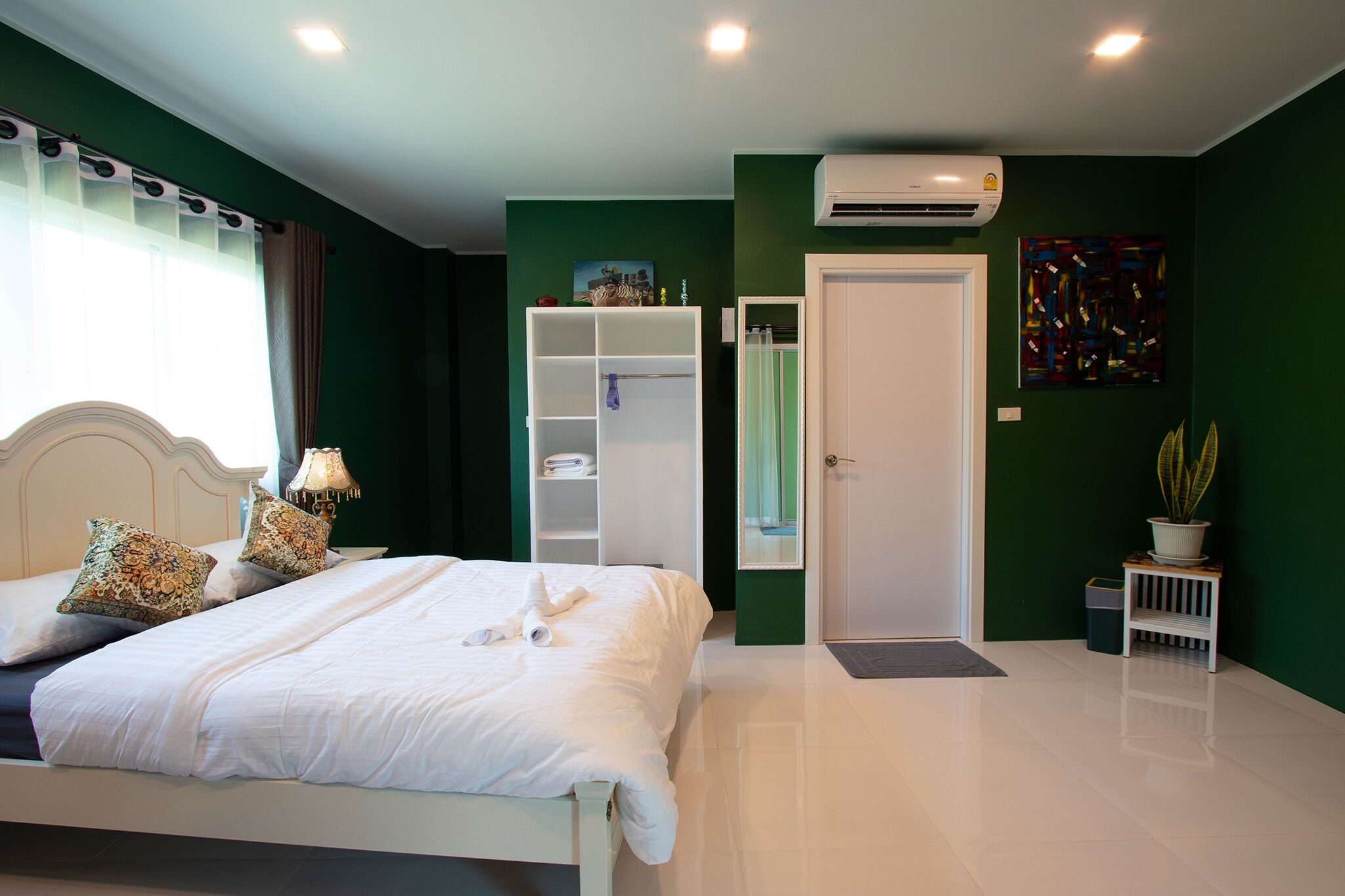 Un dormitorio ordenado con una cama, un armario, un espejo y una planta en maceta.