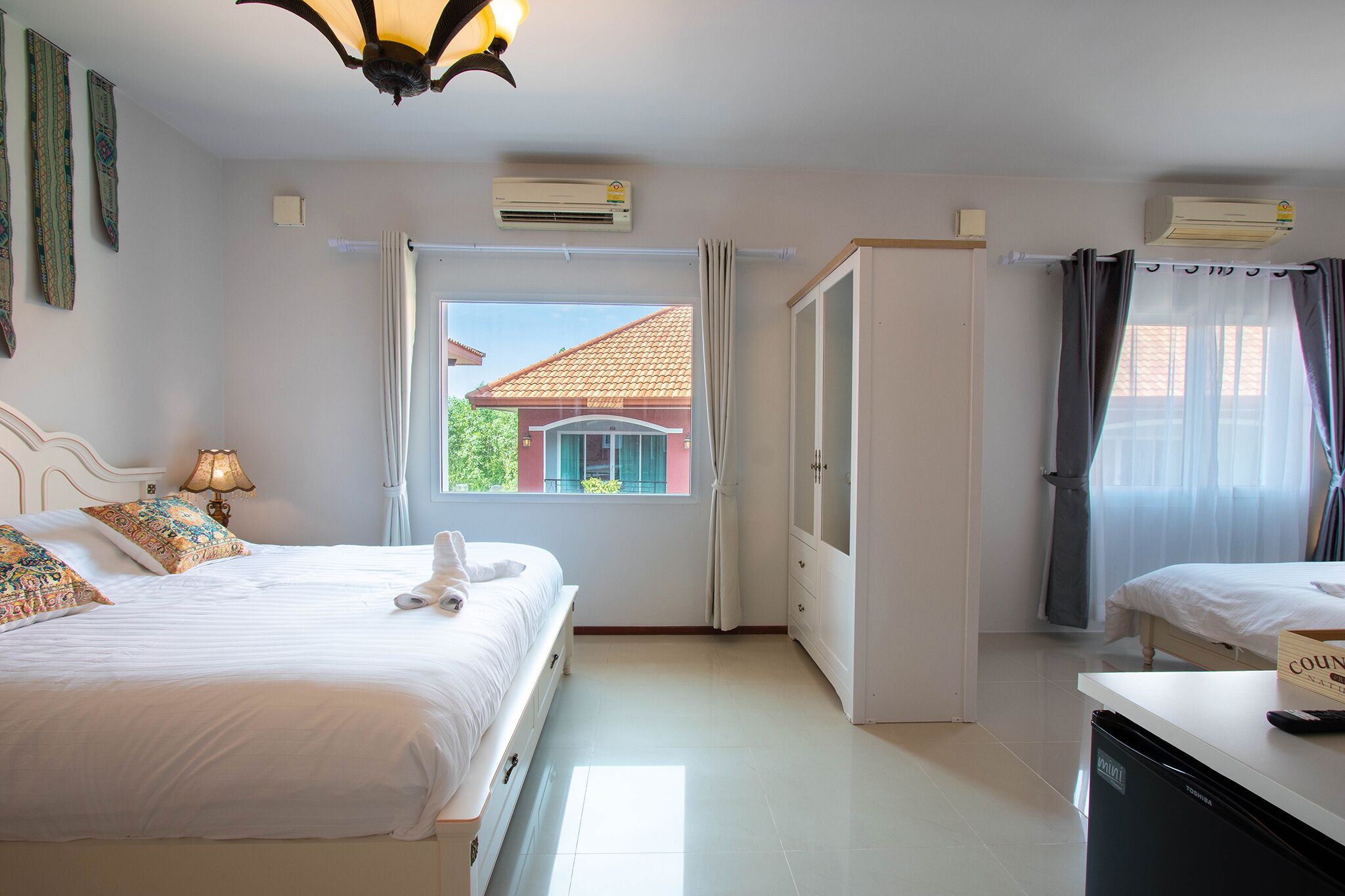 A hotel room with two beds, a wardrobe, a desk, and a window with a view of a building.