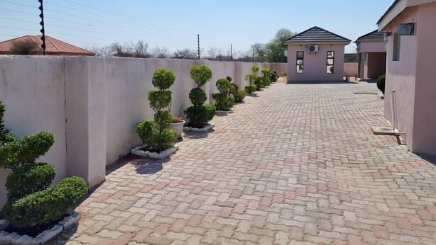 Un sendero pavimentado bordeado de arbustos podados, que lleva a un edificio con techo de tejas y un pequeño porche.