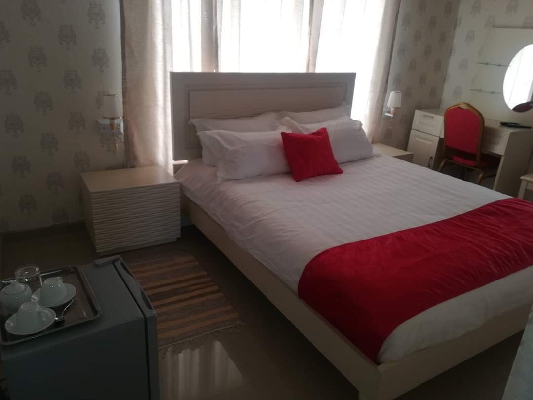 A neatly made bed with white and red bedding, a bedside table with a tray of glasses, and a chair in the corner.